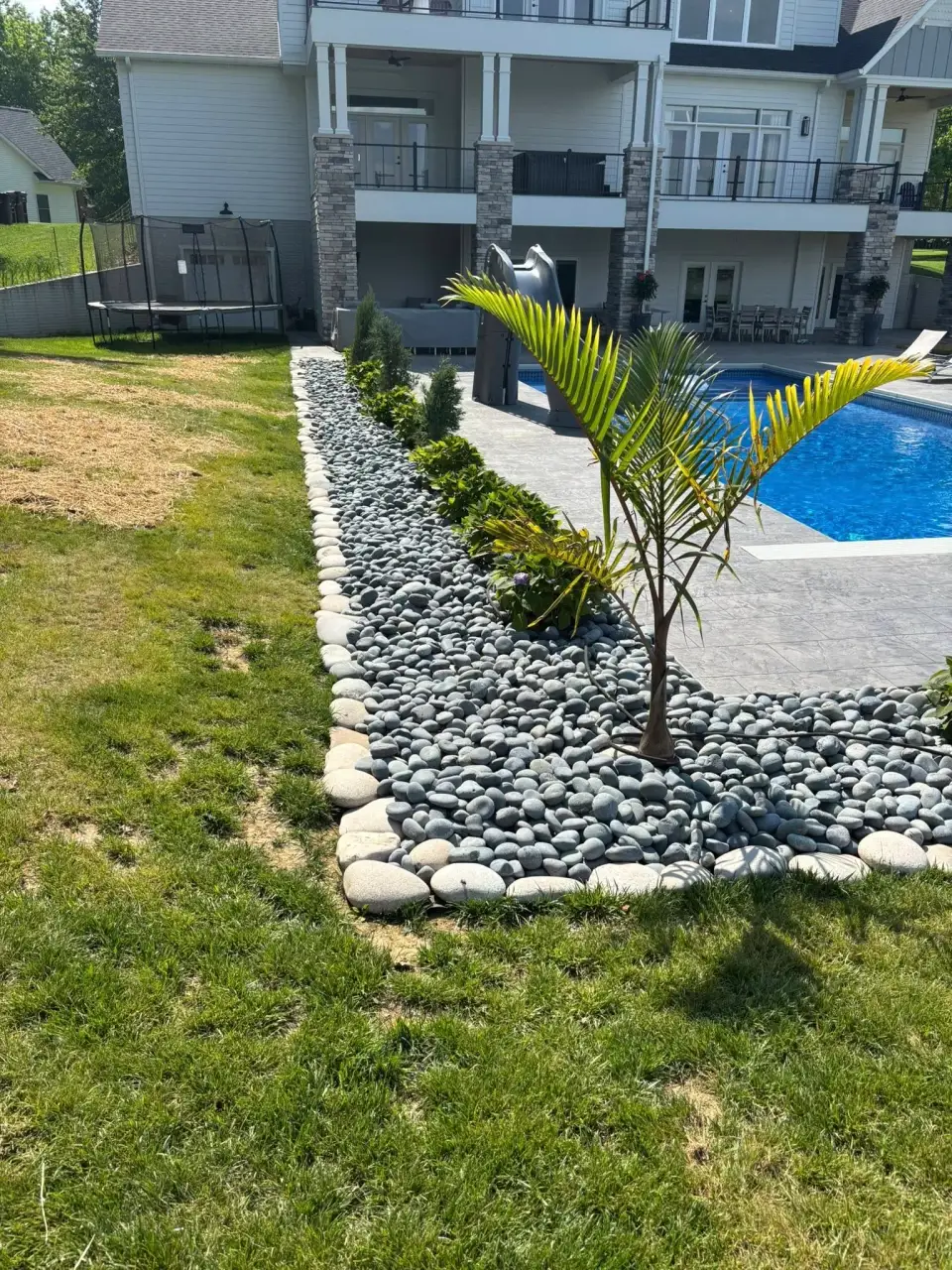 Curved garden border with shrubs and river rock beside a lawn.