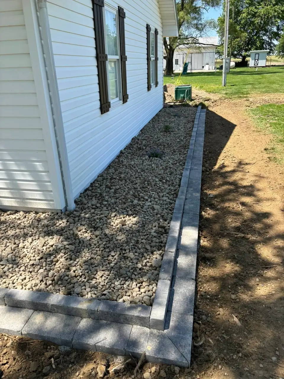 River-rock planting bed with a straight stone border beside a house.